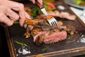 knife and fork cutting grilled beef steak